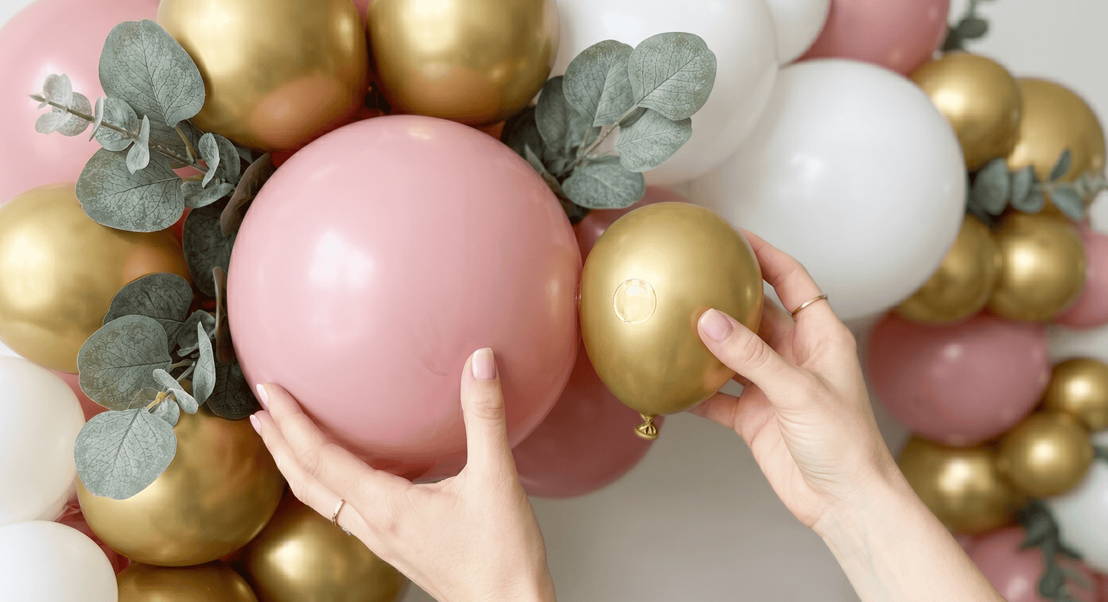 Close-up of hands arranging pink and gold balloons for a DIY balloon arch.
