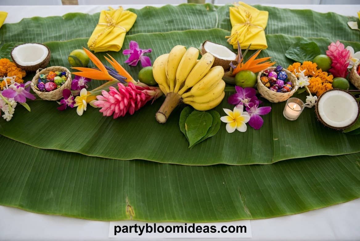 Banana leaf table runner with tropical food, white serving dishes, candles, and fresh pineapples for a luau party