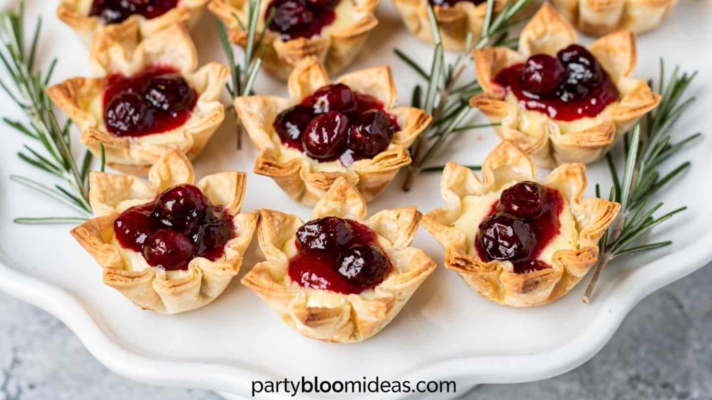 Cranberry brie bites in golden phyllo cups topped with thyme on a serving board