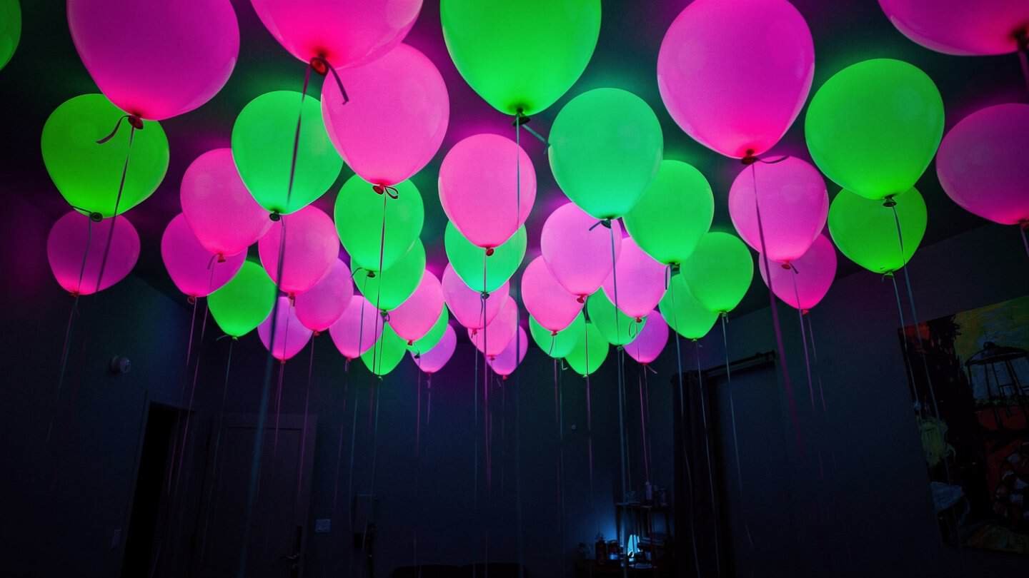 Vibrant pink and green balloon ceiling canopy glowing under blacklight
