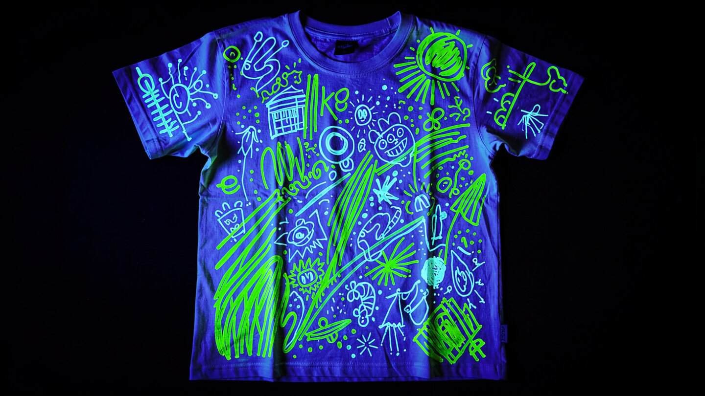 White party t-shirt covered in glowing UV marker doodles under blacklight