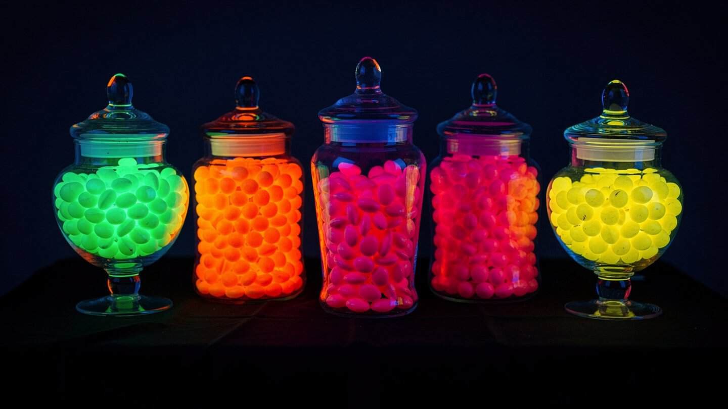 Bright neon gumballs and candy in clear glass jars for a glow party candy bar
